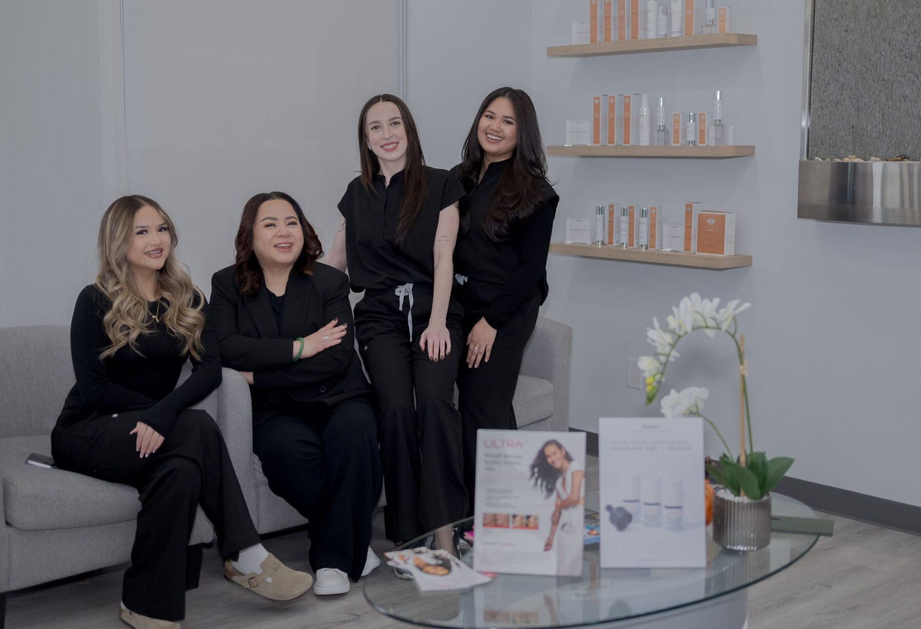 Four Kara Esthetics team members smiling together in a modern skincare and aesthetics clinic reception area.